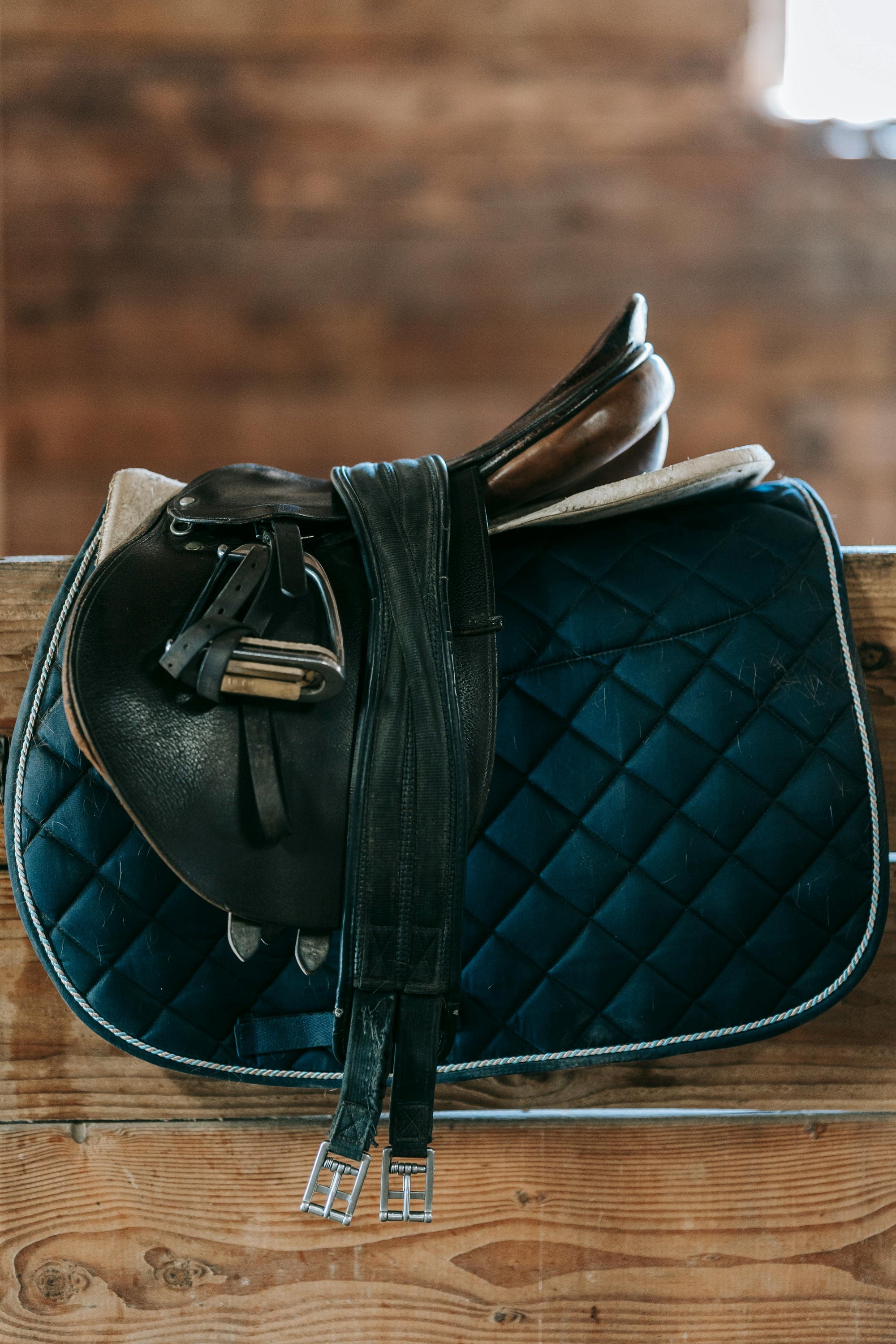 Saddle and quilted saddle pad on a wooden surface with a blurred background